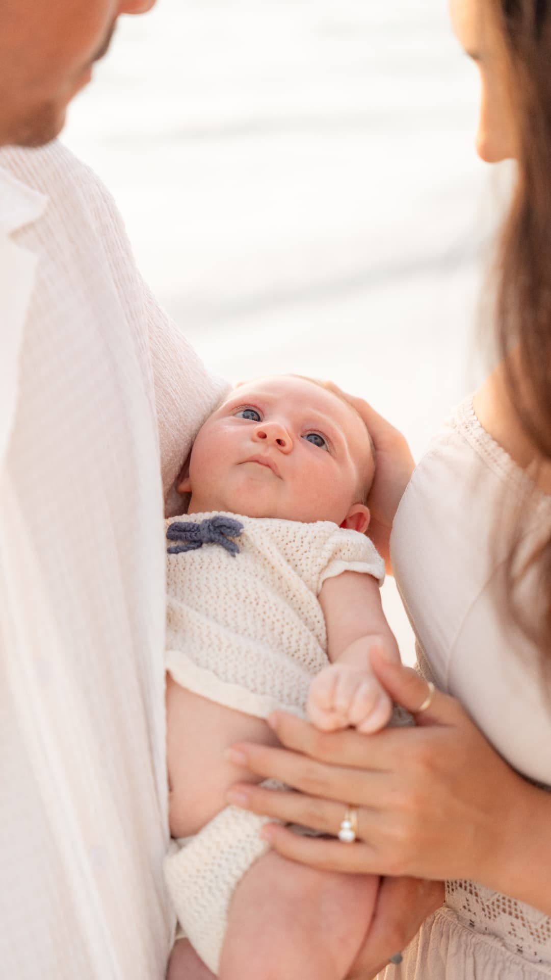 Newborn baby held between mom and dad during a beach family session