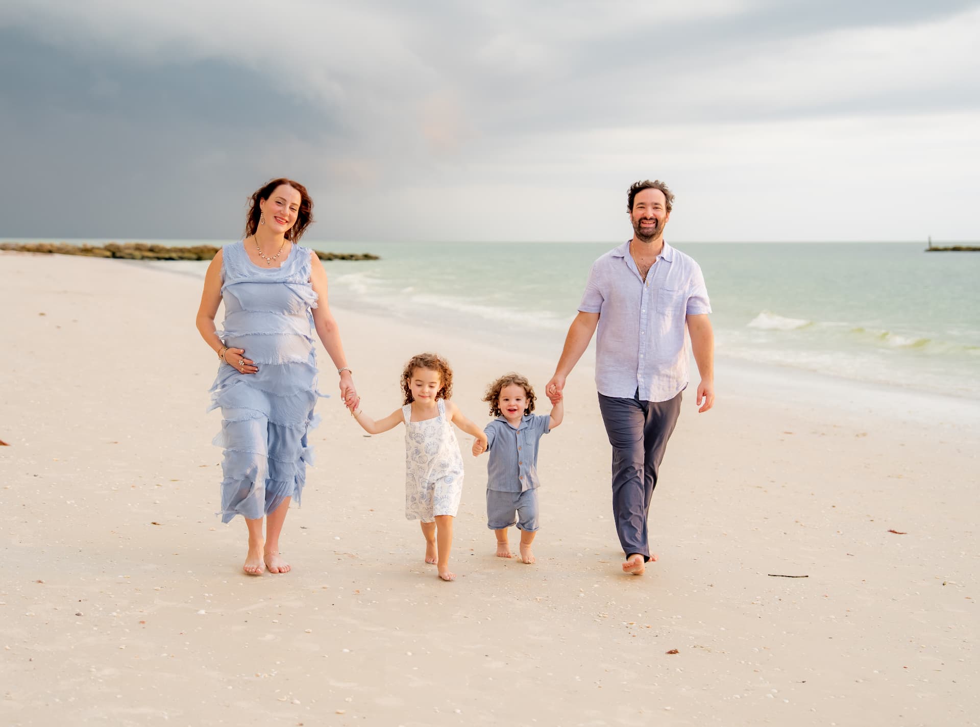 Expectant parents embracing on the shoreline at golden hour
