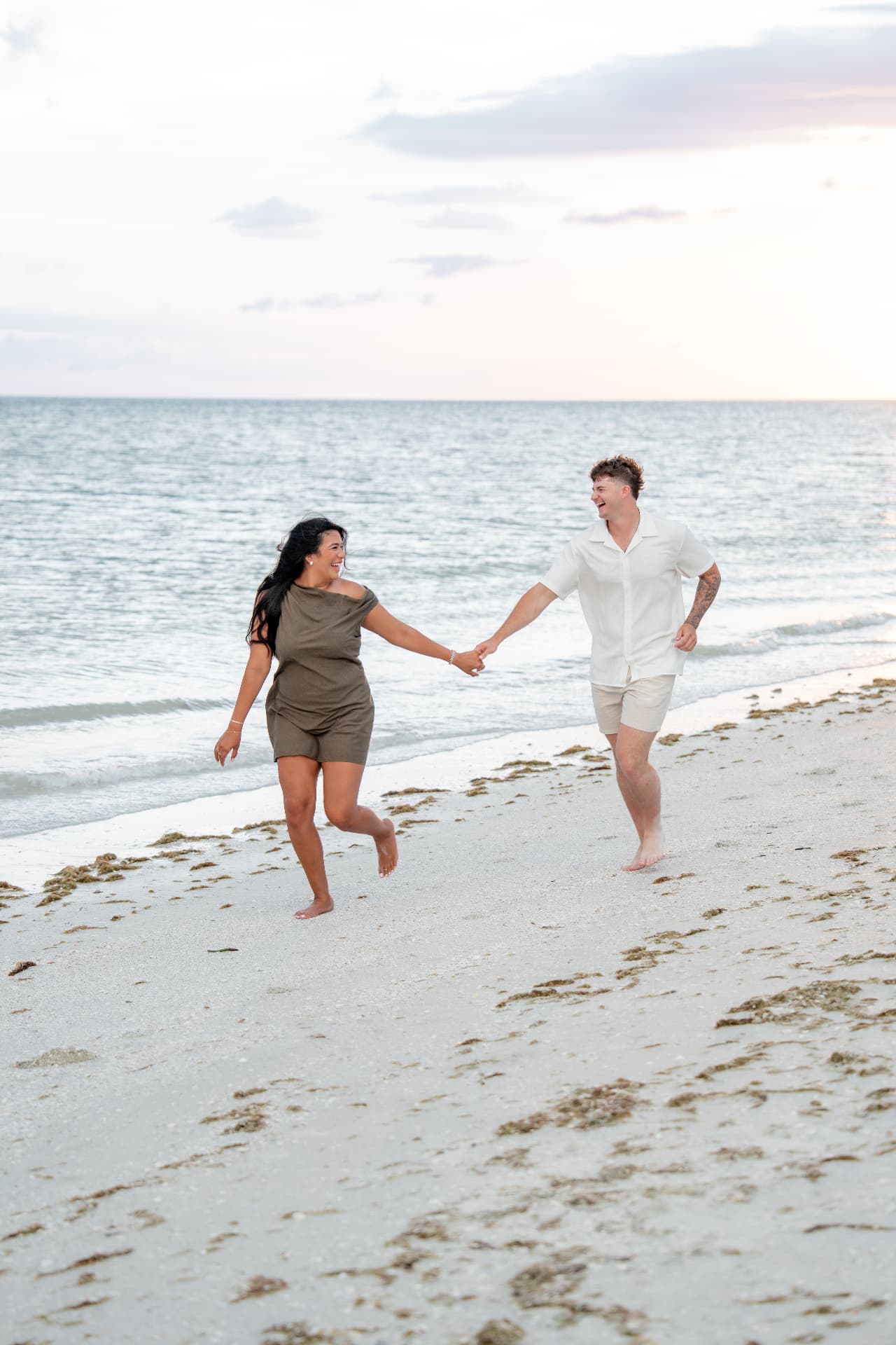 Engaged couple running hand in hand along the shoreline at dusk
