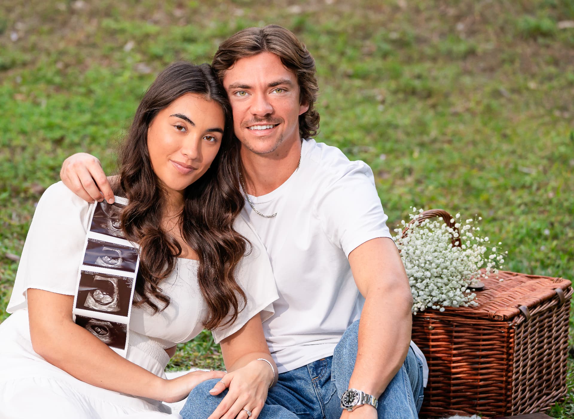 Expecting couple sitting on a picnic blanket holding ultrasound photos
