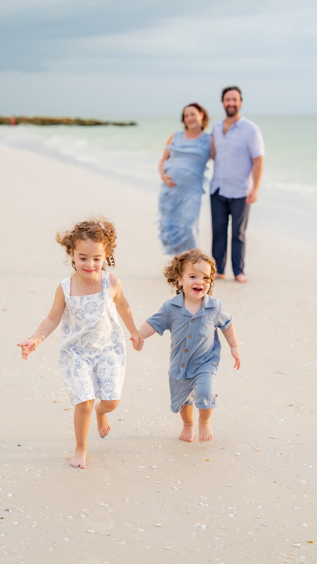 Expecting parents walking behind their two children on the beach during a maternity session