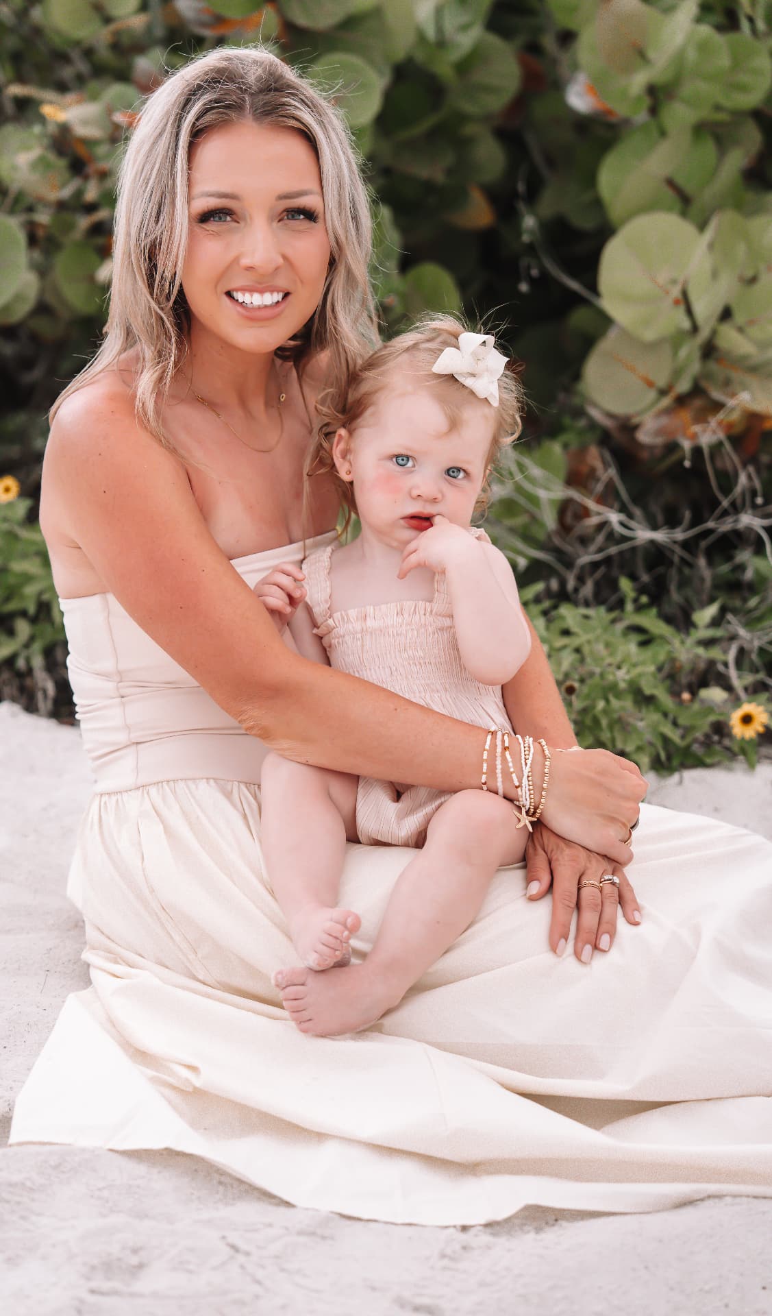 Mother holding her toddler daughter on the sand beside sea grape leaves