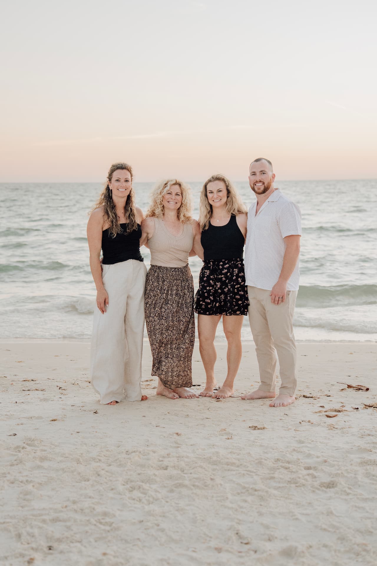 Extended family of four standing together on the beach at sunset