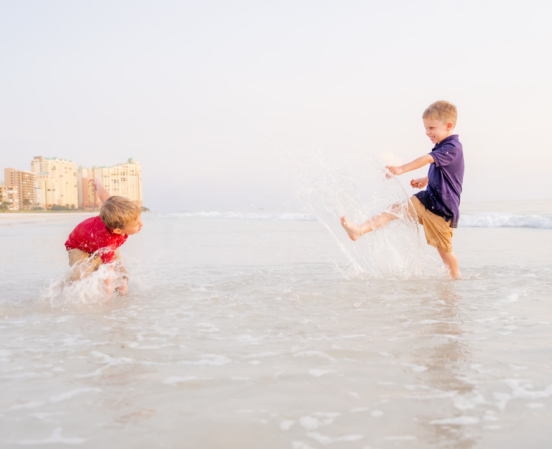 Brothers kicking up a wall of water in the surf at golden hour