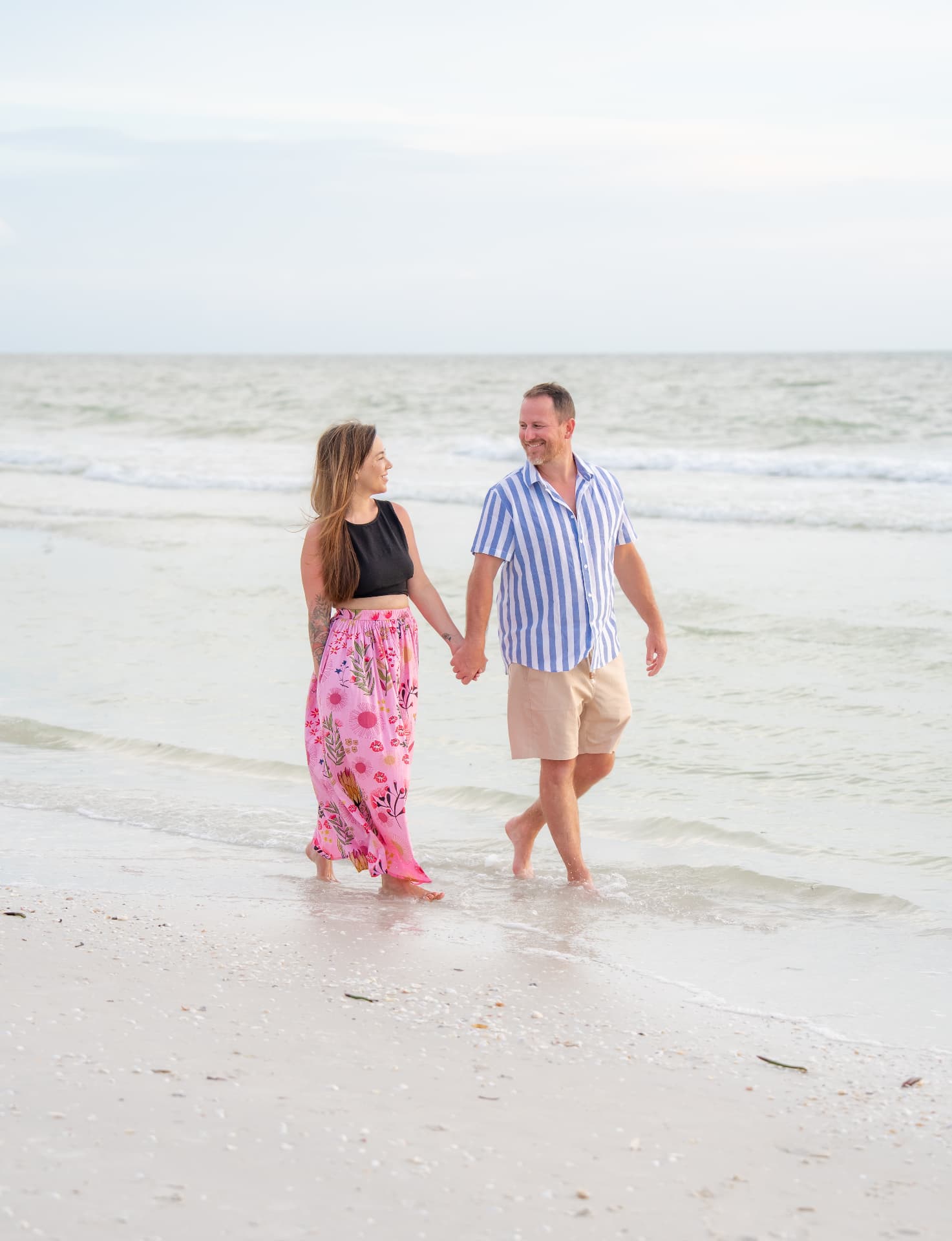 Couple walking hand in hand through the shallow surf during a relaxed beach session