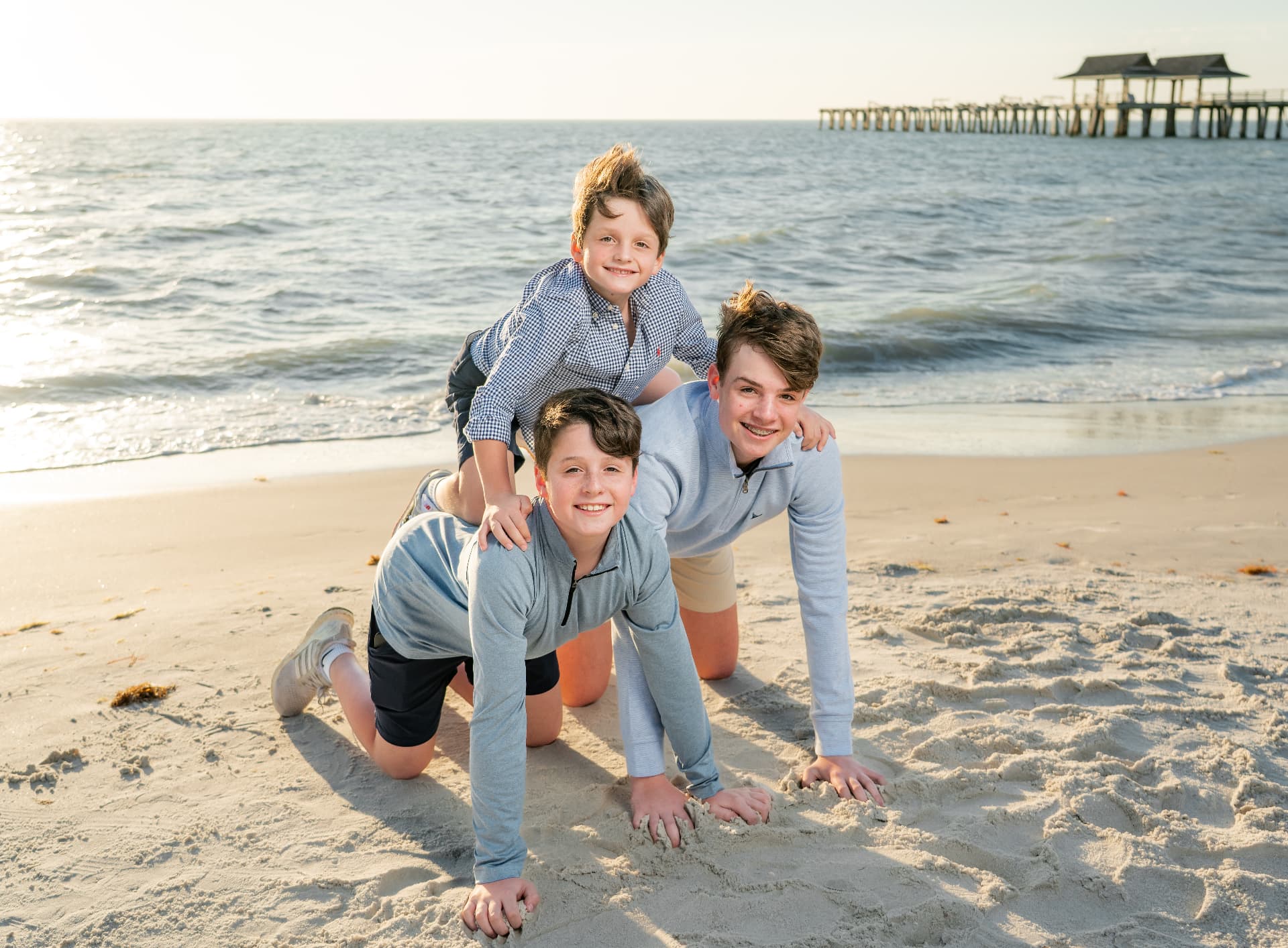 Three brothers stacked up laughing on the sand with the Naples pier behind them