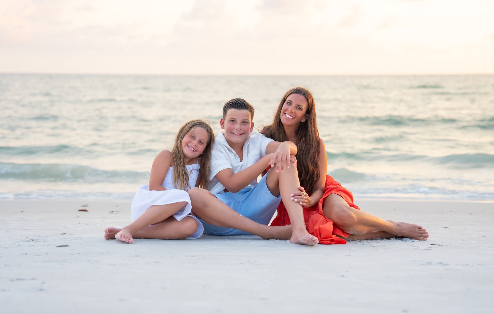 Mother and two children sitting together on the sand at sunset on Marco Island
