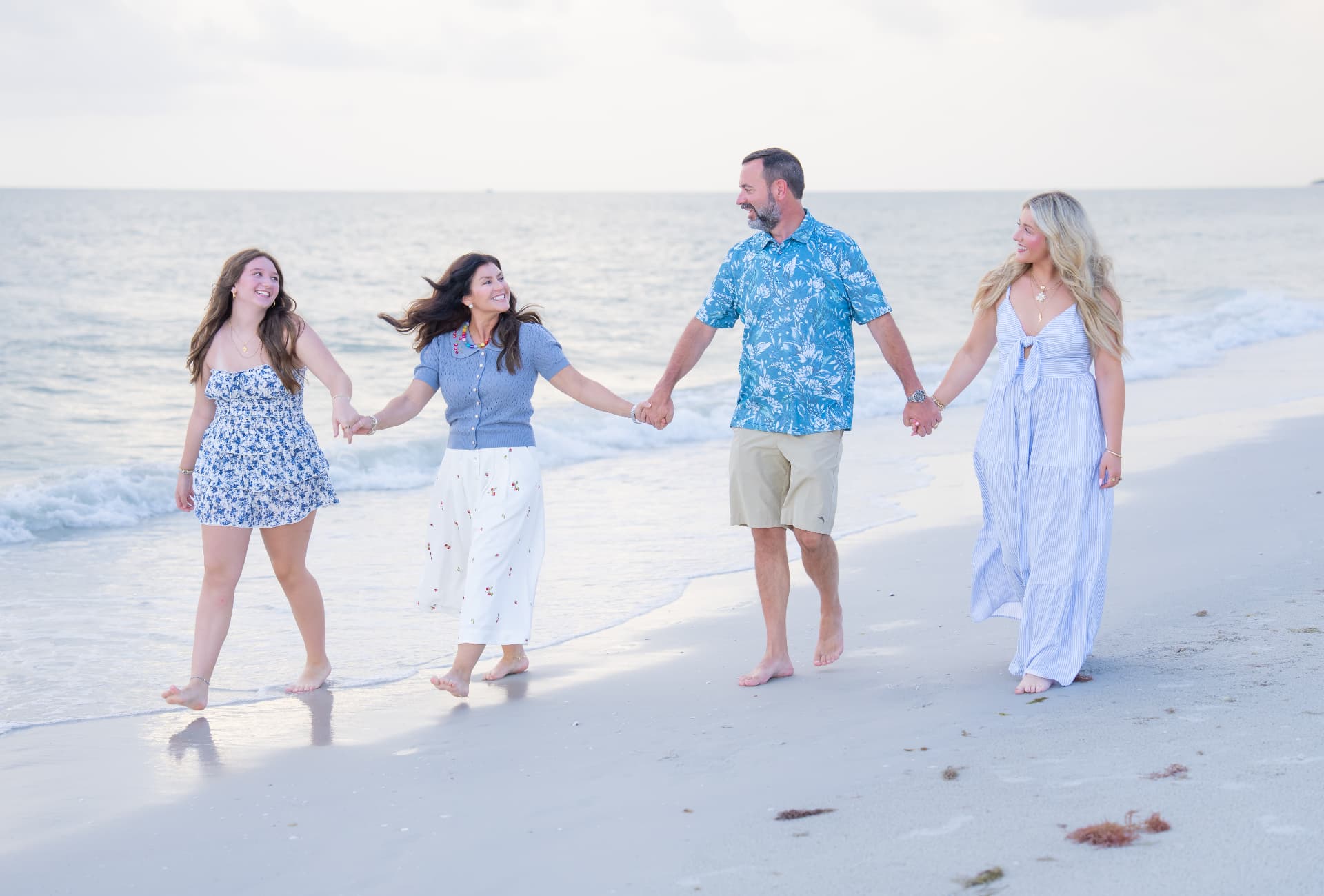 Family of four holding hands and walking through the surf at sunset