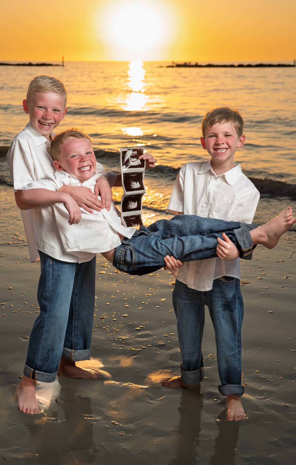 Three big brothers holding their youngest brother and ultrasound photos at sunset