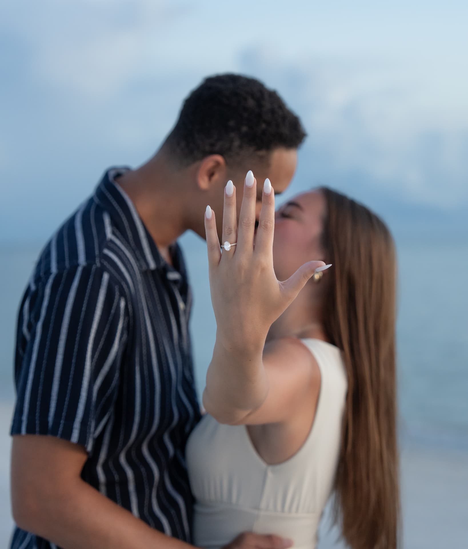 Newly engaged bride showing her ring to the camera while they kiss at blue hour