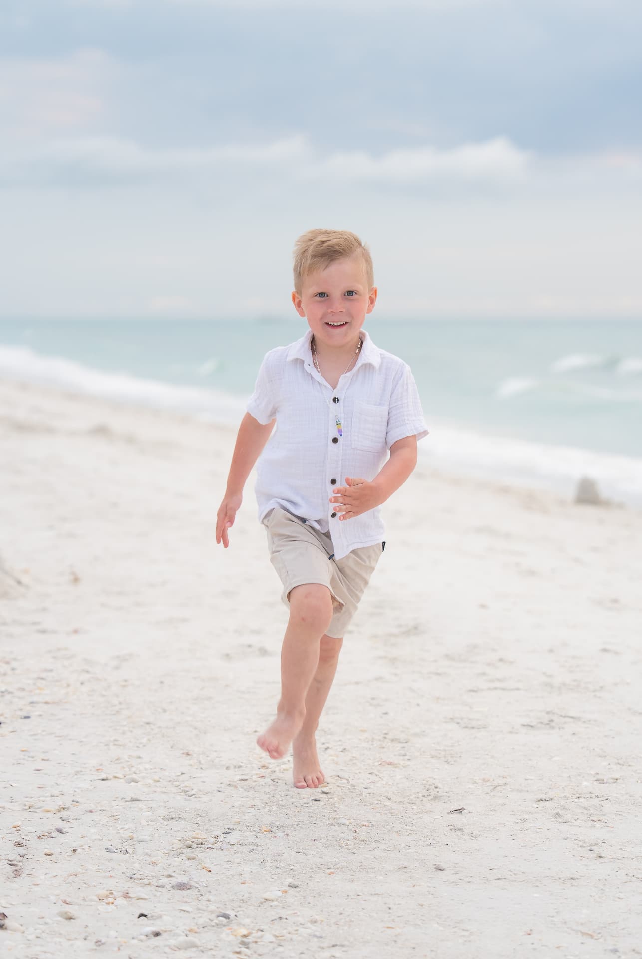Young boy running barefoot down the beach with a grin
