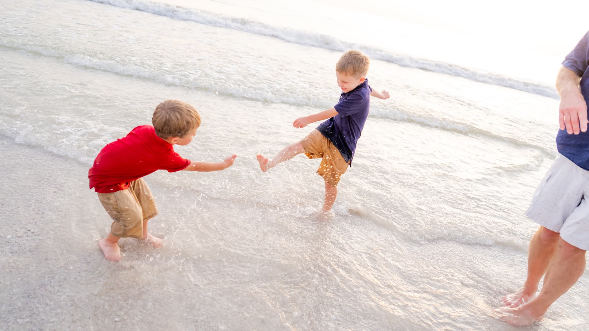 Two brothers splashing in the shallow gulf water while dad stands nearby