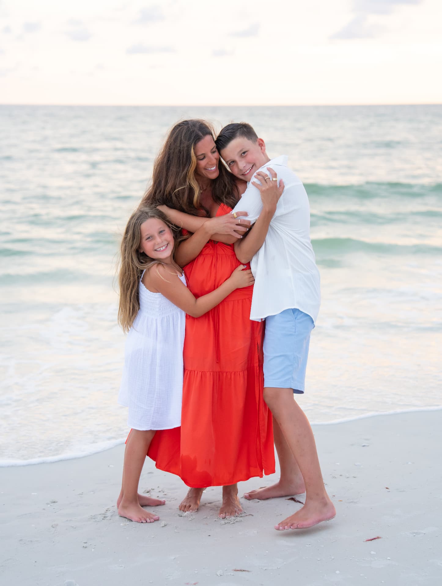 Mother hugging her son and daughter close on the beach at sunset